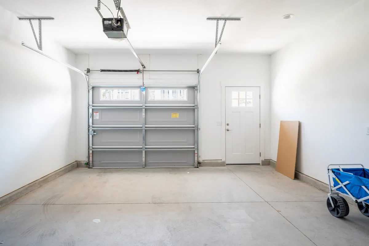 A spacious garage interior with a garage door, side door, and utility cart. The floor is uncluttered, emphasizing the ample storage and parking space.