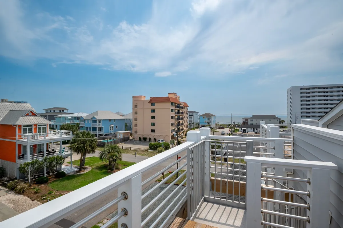 A tranquil balcony setting overlooking the ocean with a sturdy railing, nearby palm trees, and buildings in the distance. The inviting outdoor seating area captures the essence of relaxation, with sunlight glinting off the water and ample space for enjoying a sunset cocktail or a quiet morning coffee.