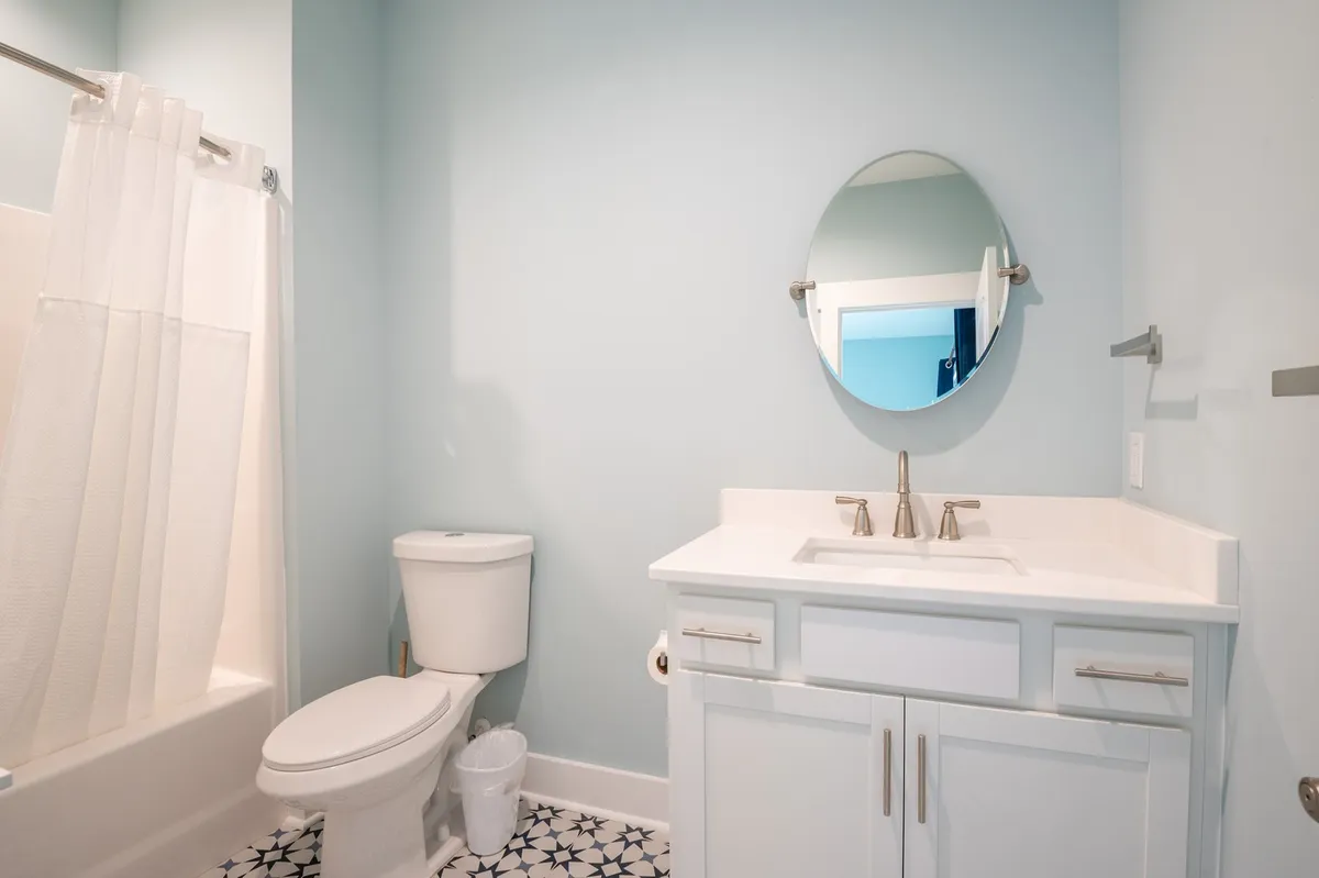 A fresh and inviting ensuite bathroom featuring a vanity sink, round mirror, toilet, and shower curtain. The space is clean and modern, ideal for personal grooming and relaxation routines.