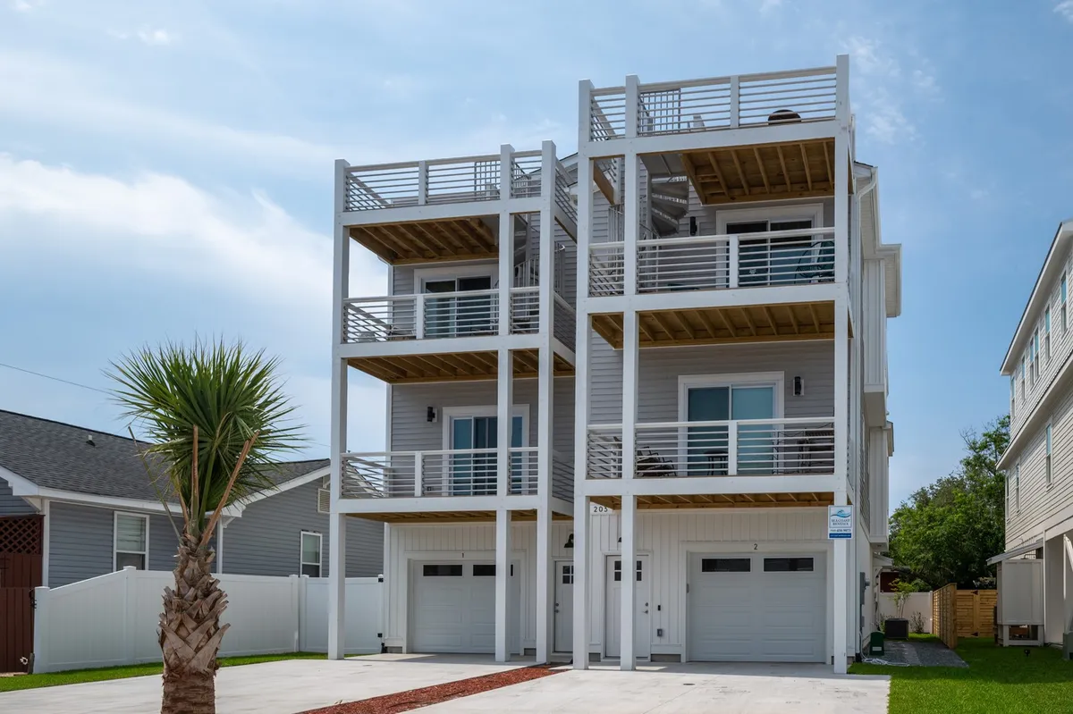 The image displays the modern exterior of a spacious beach house with sleek balconies, a prominent palm tree, and inviting outdoor spaces that hint at the nearby ocean. The cheerful mood is heightened by sunlight glinting on the balconies, suggesting perfect spots to relax, socialize, or take in the sea air.