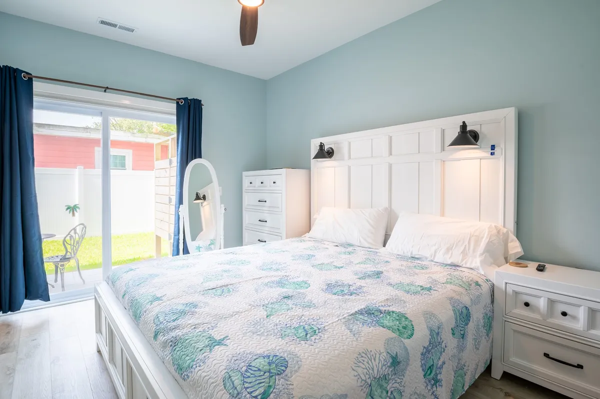 A tranquil bedroom with marine-themed bedding, large window with sliding door, and crisp white furniture. The space exudes calm and offers the perfect retreat for relaxation or enjoying morning coffee in privacy.