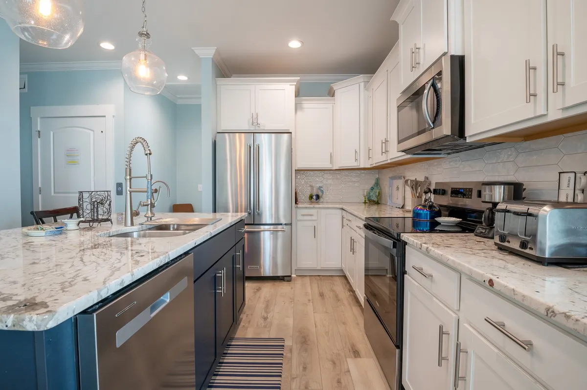 A modern kitchen with granite countertops, stainless steel appliances, blue cabinetry, and elegant hanging pendant lights. The setup suggests a space designed for both gourmet cooking and entertaining.