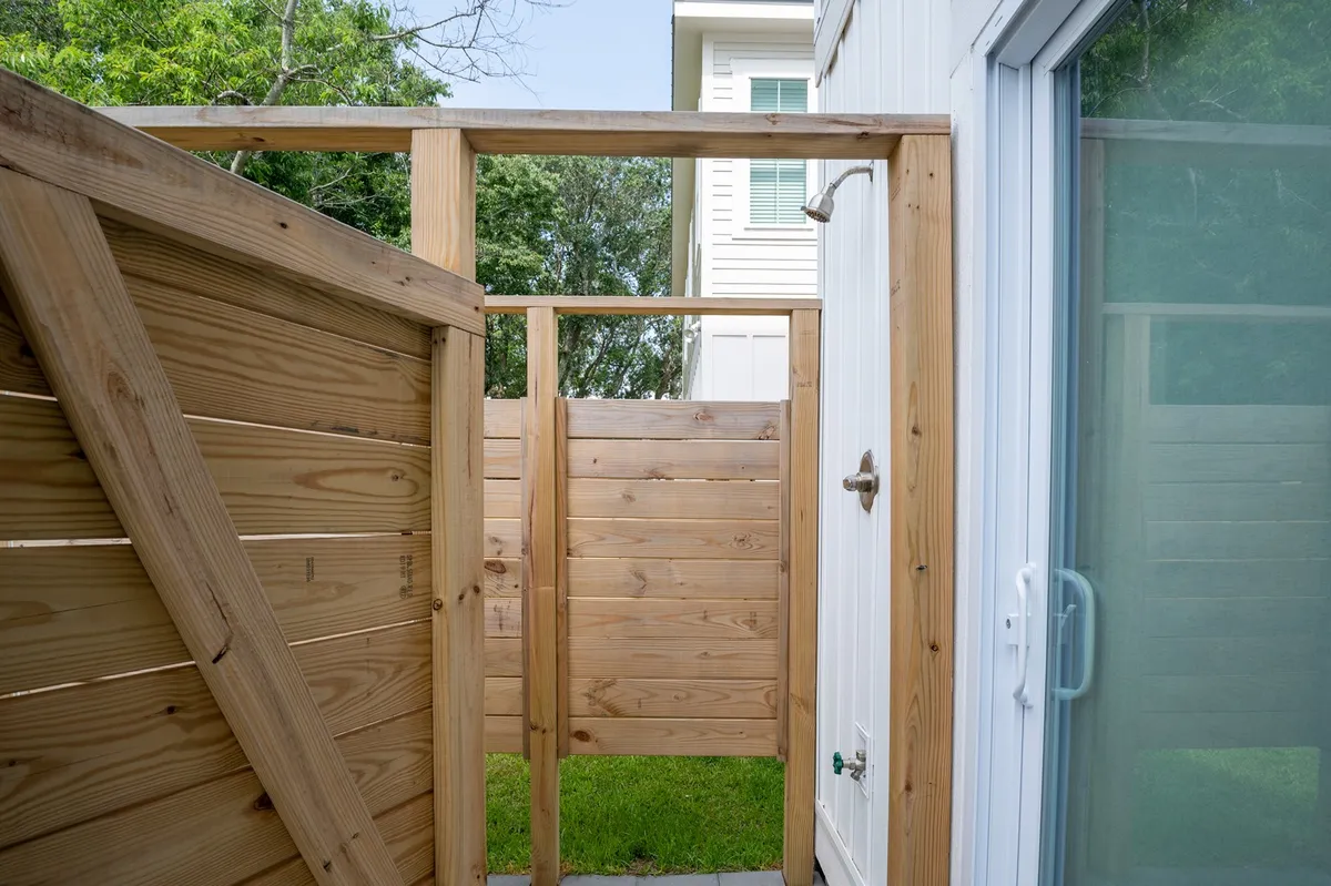 This image showcases an outdoor shower enclosed by wooden fencing, set beside a lush patch of green grass. The shower fixture is visible, hinting at both privacy and refreshment after outside activities.