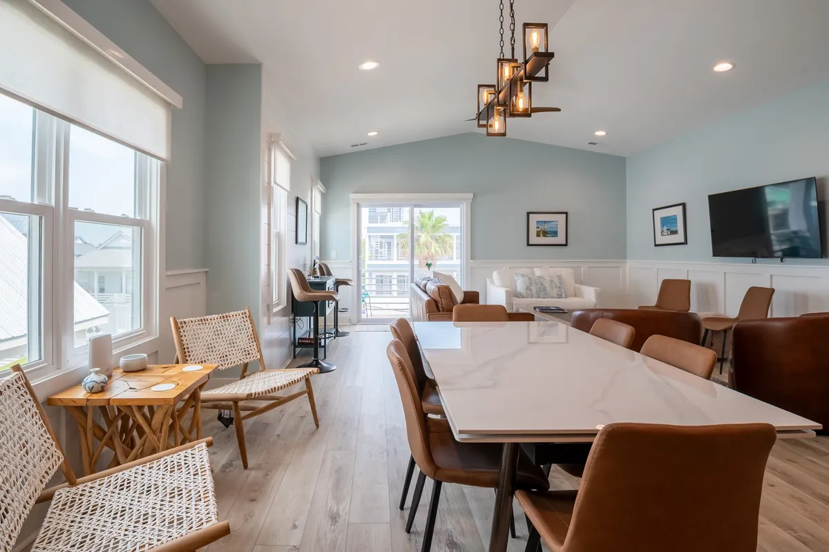 A spacious dining area with a large table, comfortable seating, expansive windows, and a striking chandelier. Sunlight pours in, creating a warm and welcoming mood, ideal for group meals and celebrations.