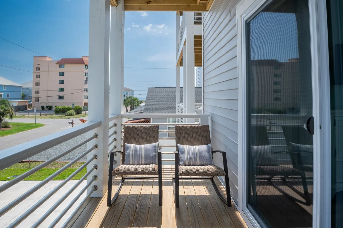 A serene balcony area with two wicker chairs and decorative cushions set against a sturdy balcony railing. The scene suggests a quiet place to enjoy the fresh air, gaze at the sunrise, or stargaze at night, directly linking indoor comfort with the outdoors.
