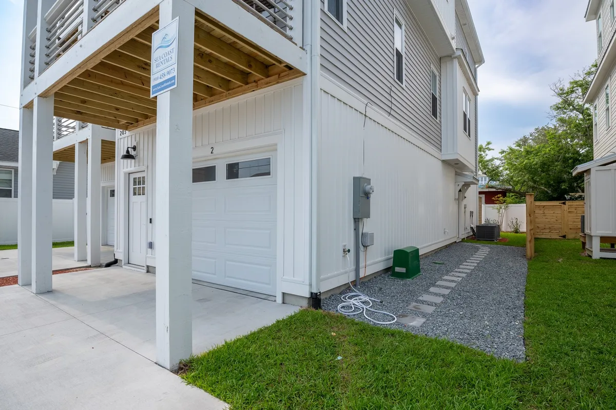 The image shows the front exterior of the property with a welcoming garage door, clear signage, a gravel pathway, and a lush green lawn. The scene suggests the arrival experience at Lone Star Breeze, where groups can gather before heading out to explore or unwind after a day of activities.