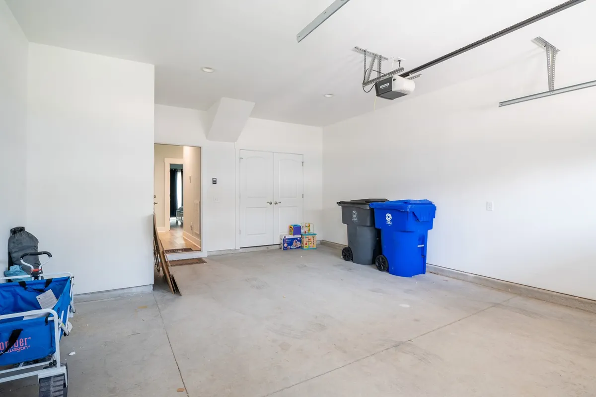 A functional garage space equipped with a garage door opener, blue recycling bin, and some toys on the floor, offering ample storage for beach gear, bicycles, and other adventure essentials.
